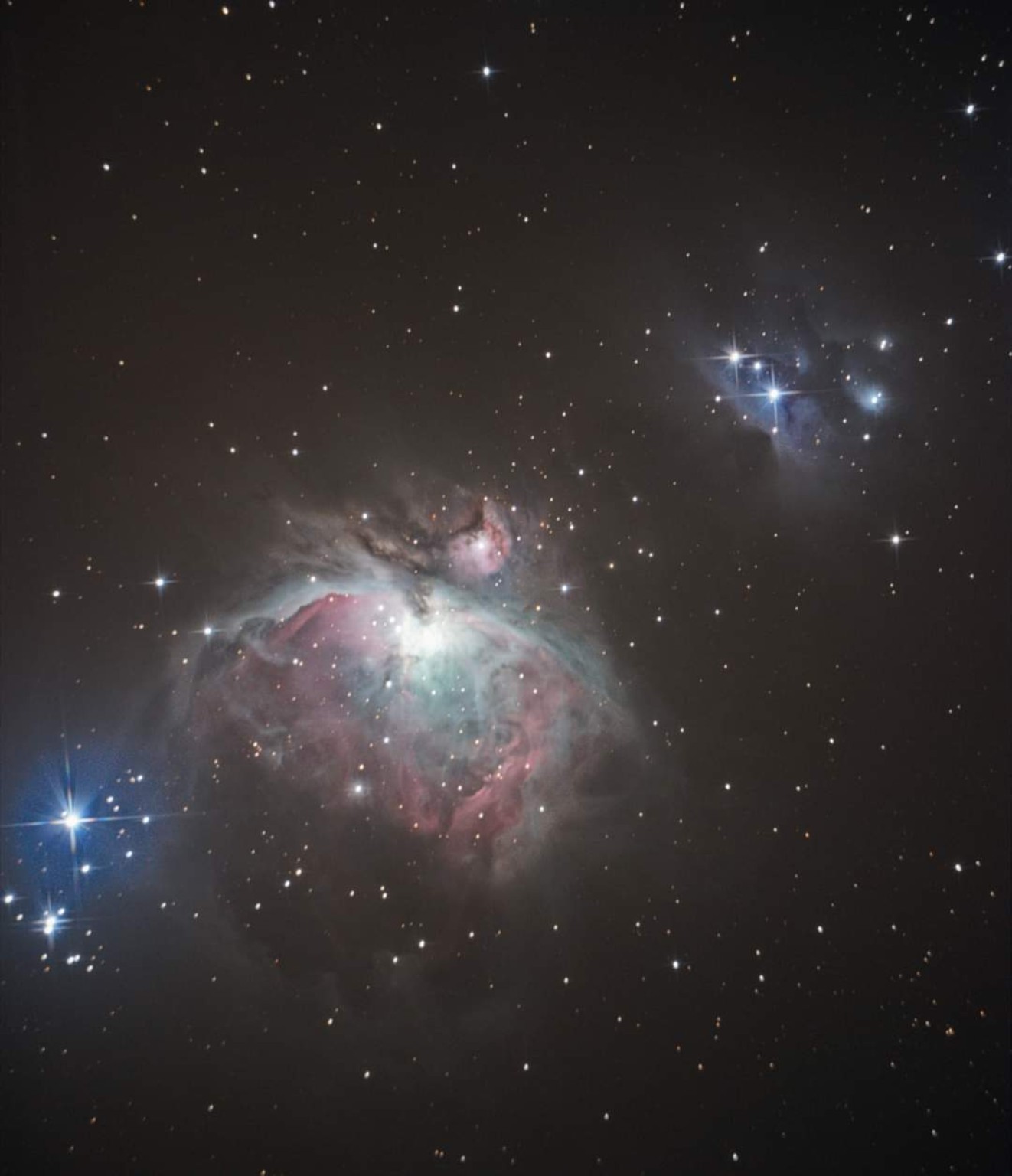 Dennis Gorican’s photograph of Orion: the luminous pink and pale blue M42 nebula below centre, the smaller M43 just above it, and a blue reflection-nebula region towards the upper right.